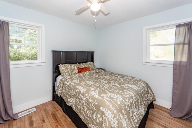 bedroom with multiple windows, a textured ceiling, light hardwood / wood-style floors, and ceiling fan