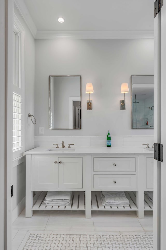 bathroom with double vanity, crown molding, walk in shower, and a sink