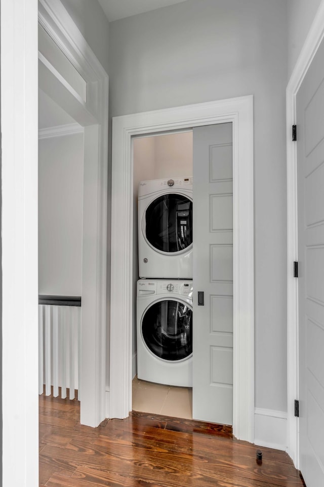 laundry room featuring stacked washer / dryer, laundry area, baseboards, and wood finished floors