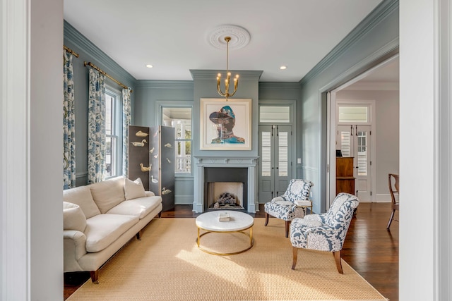 living area featuring crown molding, wood finished floors, a fireplace with flush hearth, and an inviting chandelier