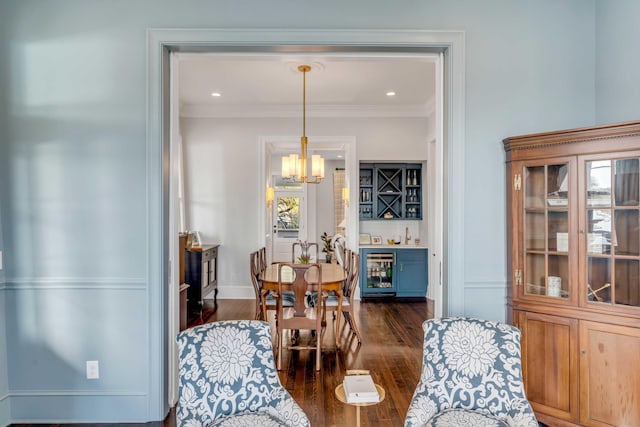 dining space featuring beverage cooler, a bar, a notable chandelier, dark wood finished floors, and ornamental molding