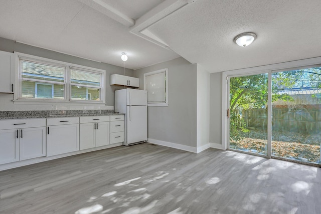 kitchen with white cabinetry, freestanding refrigerator, light wood-style floors, baseboards, and light stone countertops