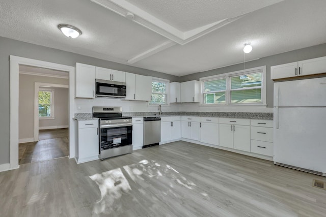 kitchen with a wealth of natural light, white cabinets, stainless steel appliances, and light wood-type flooring