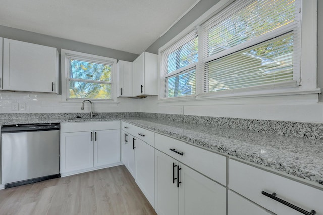 kitchen featuring a sink, light stone counters, stainless steel dishwasher, light wood-style floors, and white cabinets