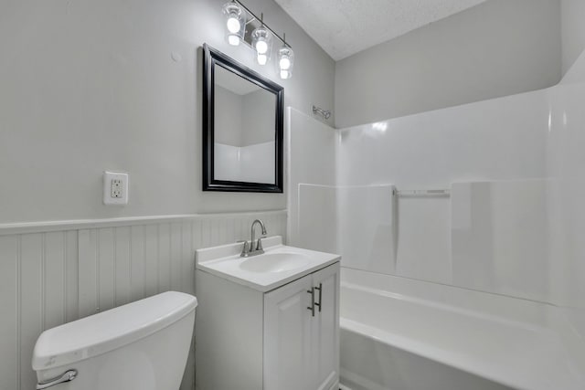 full bathroom with vanity, wainscoting, a textured ceiling, bathing tub / shower combination, and toilet