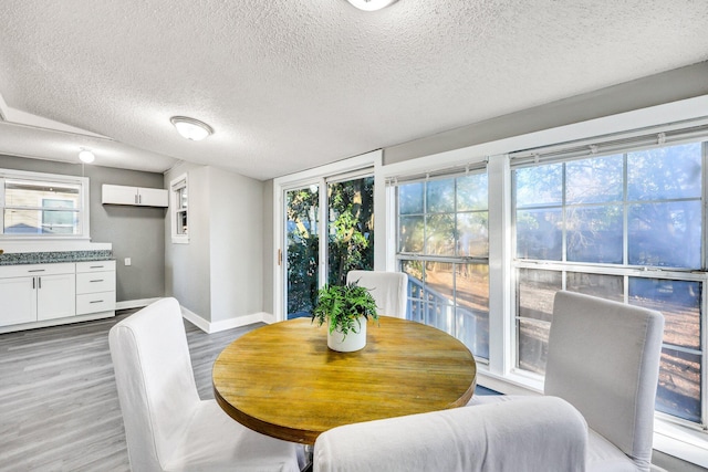 dining space with a textured ceiling, baseboards, and light wood-style floors