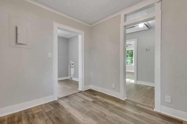 empty room with baseboards, a textured ceiling, wood finished floors, and ornamental molding