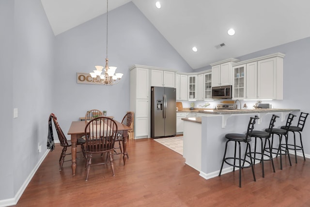 kitchen with stainless steel appliances, high vaulted ceiling, a breakfast bar area, a peninsula, and white cabinetry