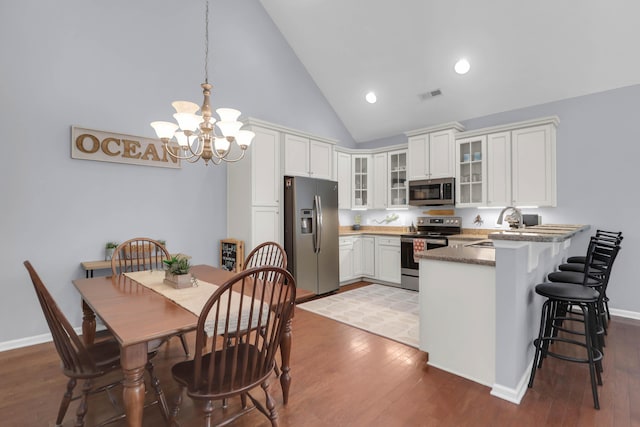 kitchen featuring appliances with stainless steel finishes, a peninsula, high vaulted ceiling, a sink, and a chandelier