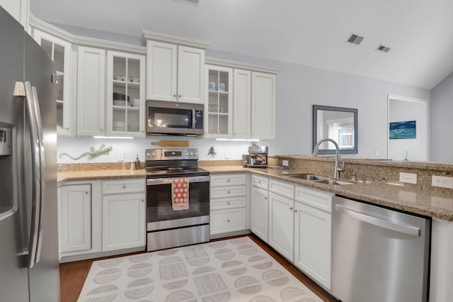 kitchen featuring appliances with stainless steel finishes, a sink, light stone countertops, light wood finished floors, and white cabinetry