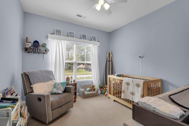carpeted bedroom with a ceiling fan and a nursery area