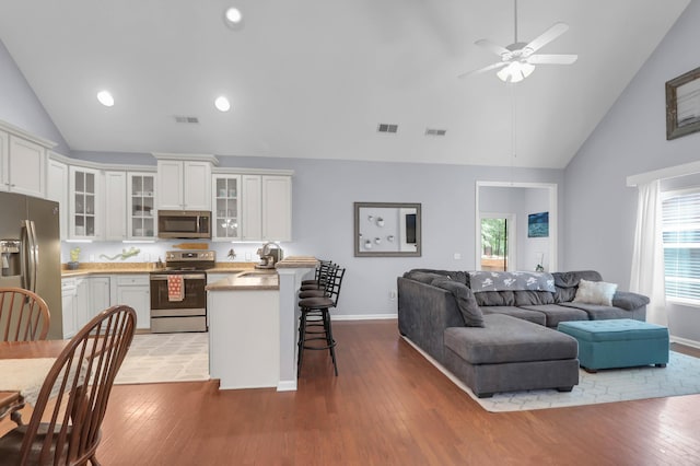 kitchen featuring appliances with stainless steel finishes, a kitchen bar, a peninsula, white cabinetry, and high vaulted ceiling