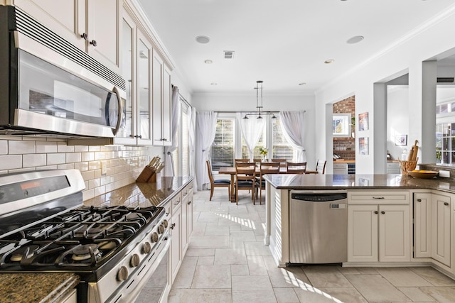 kitchen featuring crown molding, hanging light fixtures, dark stone countertops, stainless steel appliances, and decorative backsplash