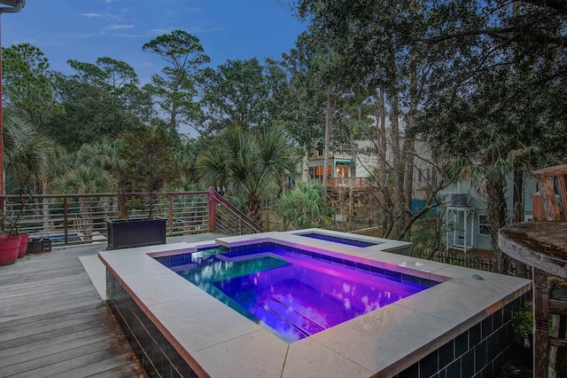 pool at dusk featuring an in ground hot tub and a deck