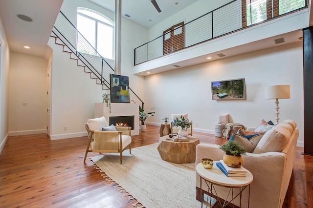 living room with ceiling fan, light hardwood / wood-style flooring, and a high ceiling