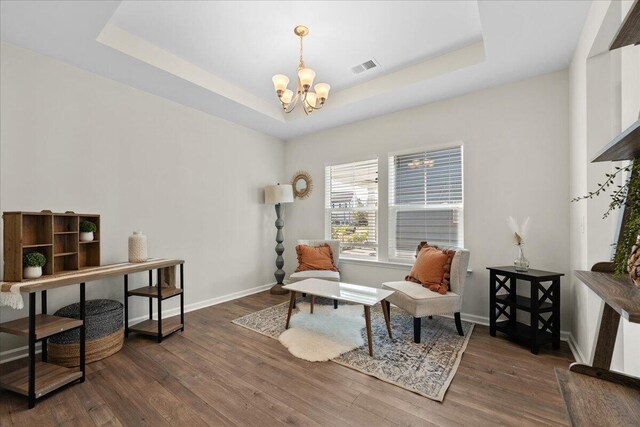 living area with a notable chandelier, a tray ceiling, and dark wood-type flooring