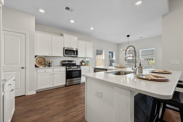 kitchen with dark wood-type flooring, an island with sink, stainless steel appliances, sink, and white cabinets