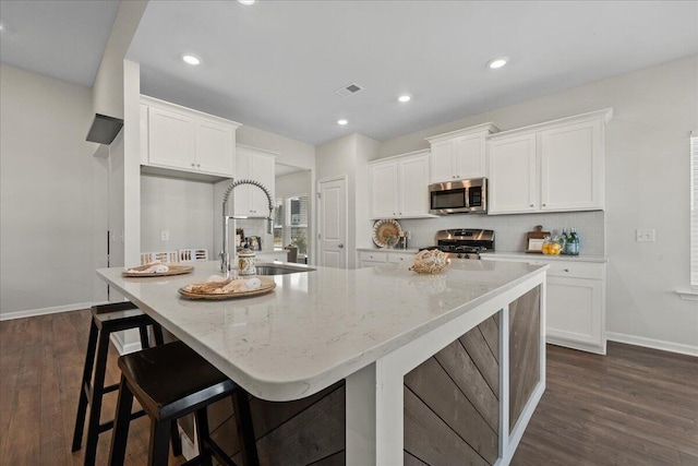 kitchen featuring white cabinets, stainless steel appliances, dark wood-type flooring, and a large island with sink