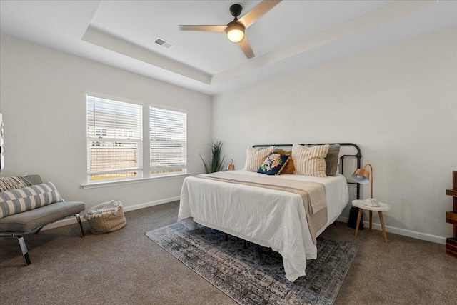 bedroom featuring ceiling fan, a tray ceiling, and dark carpet