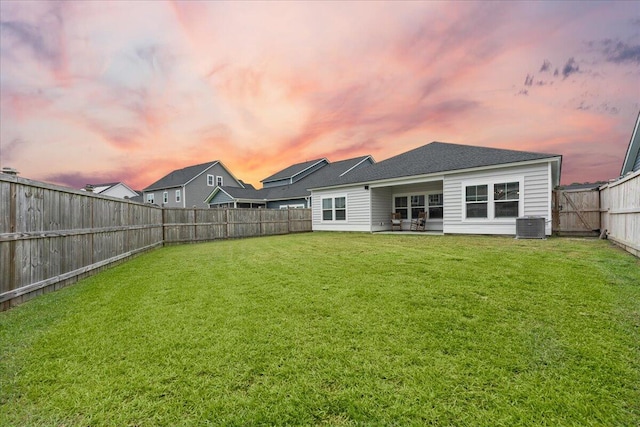 back house at dusk featuring central air condition unit, a patio, and a lawn