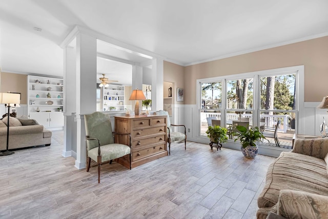 living room featuring built in shelves, light hardwood / wood-style floors, ceiling fan, and ornamental molding