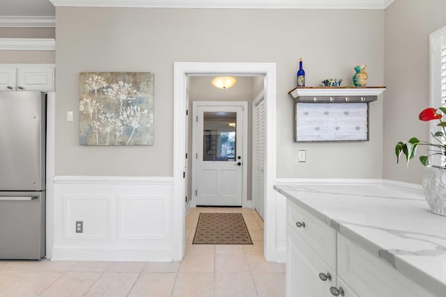 interior space with white cabinetry, stainless steel fridge, crown molding, and light stone countertops