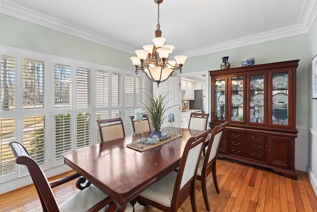 dining area with crown molding, light wood-type flooring, and an inviting chandelier