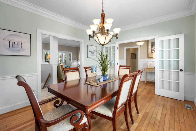 dining room with ornamental molding, french doors, light hardwood / wood-style floors, and an inviting chandelier