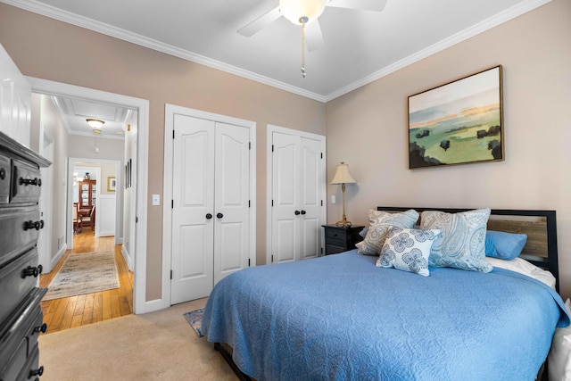 bedroom featuring ceiling fan, ornamental molding, light carpet, and two closets