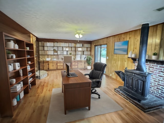 office area featuring ceiling fan, a wood stove, light hardwood / wood-style floors, and wood walls