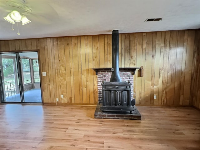 unfurnished living room featuring hardwood / wood-style floors, wooden walls, ceiling fan, and a wood stove