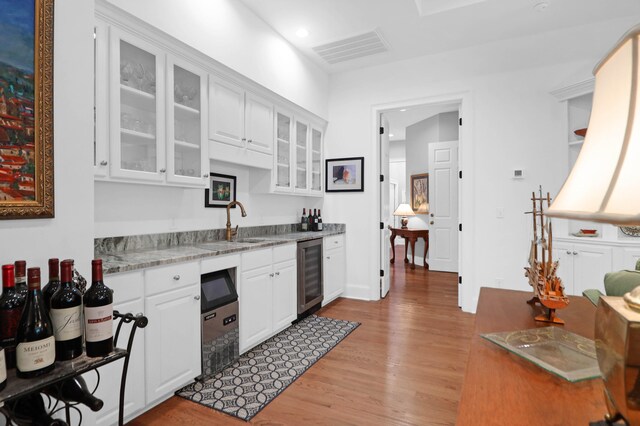 kitchen with wine cooler, sink, white cabinetry, light hardwood / wood-style flooring, and light stone countertops