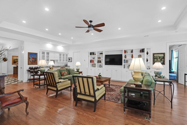 living room with a raised ceiling, ornamental molding, hardwood / wood-style floors, and ceiling fan