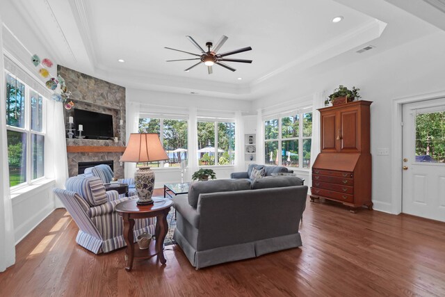 living room featuring dark hardwood / wood-style floors, ceiling fan, a tray ceiling, and a stone fireplace