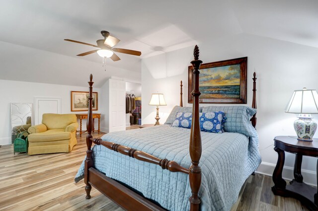 bedroom featuring ceiling fan, light hardwood / wood-style floors, vaulted ceiling, and a walk in closet