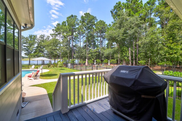 wooden deck featuring a patio area, a water view, grilling area, a yard, and a fenced in pool