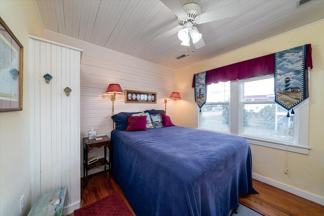 bedroom with wood walls, ceiling fan, and dark hardwood / wood-style floors