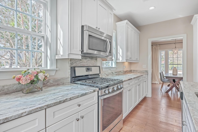 kitchen featuring white cabinetry, light wood-type flooring, light stone counters, and appliances with stainless steel finishes