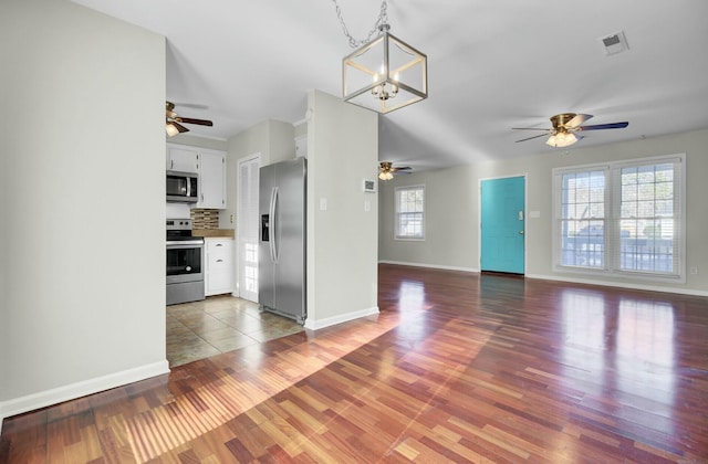 unfurnished living room featuring ceiling fan with notable chandelier, visible vents, baseboards, and wood finished floors