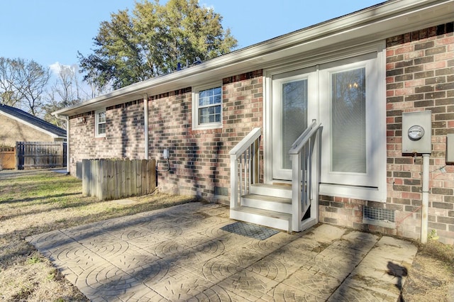 view of exterior entry with a patio area, fence, and brick siding