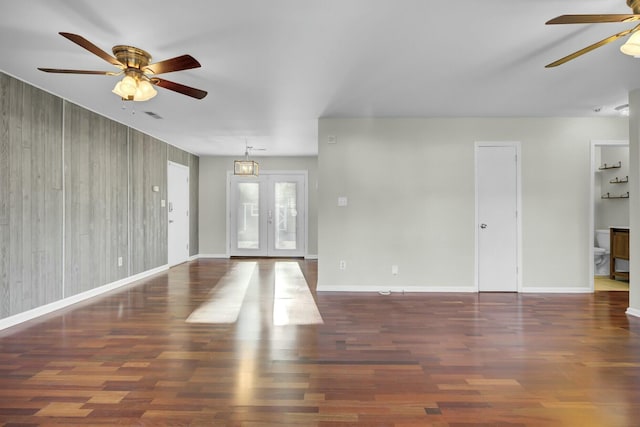 unfurnished living room with wood walls, wood finished floors, a ceiling fan, and baseboards