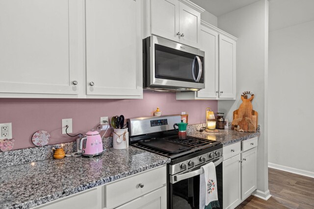 kitchen with dark stone countertops, appliances with stainless steel finishes, dark wood-type flooring, and white cabinetry