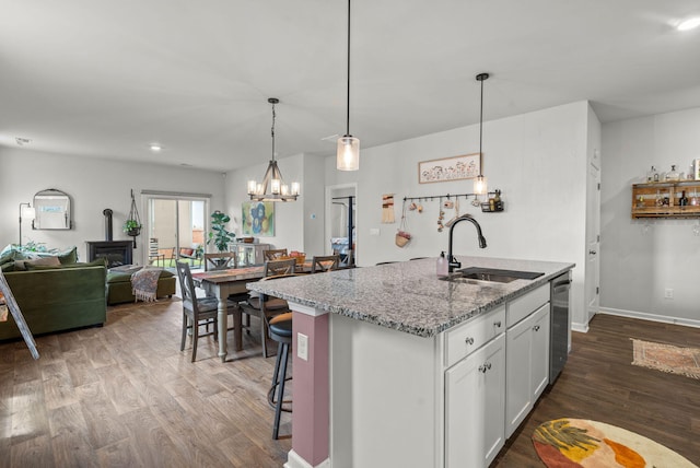 kitchen with white cabinetry, an inviting chandelier, light stone countertops, wood-type flooring, and sink