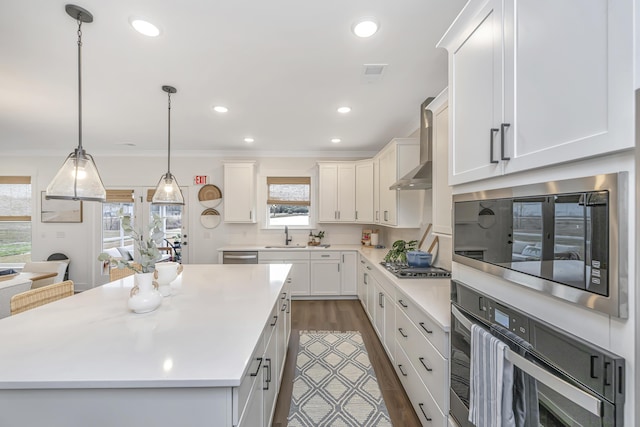 kitchen featuring appliances with stainless steel finishes, tasteful backsplash, wall chimney exhaust hood, decorative light fixtures, and a center island