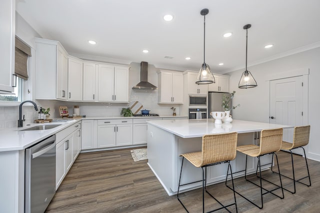 kitchen featuring stainless steel appliances, sink, wall chimney range hood, decorative light fixtures, and a center island