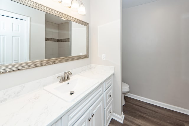 bathroom with hardwood / wood-style floors, vanity, toilet, and a tile shower