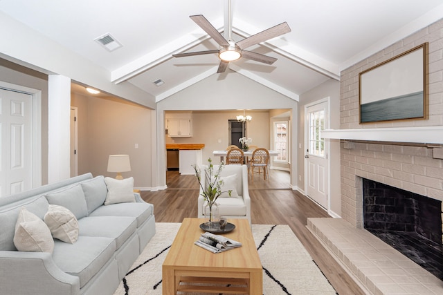 living room featuring a fireplace, ceiling fan with notable chandelier, light hardwood / wood-style flooring, and vaulted ceiling with beams