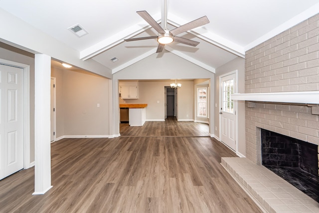 unfurnished living room featuring a brick fireplace, wood-type flooring, ceiling fan with notable chandelier, and lofted ceiling with beams