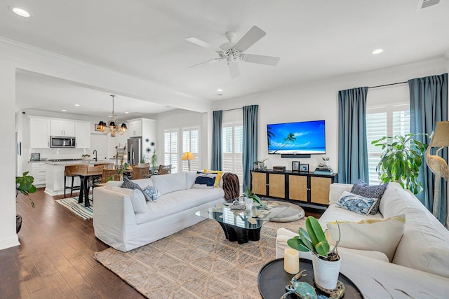 living room with ornamental molding, a healthy amount of sunlight, ceiling fan with notable chandelier, and dark hardwood / wood-style flooring