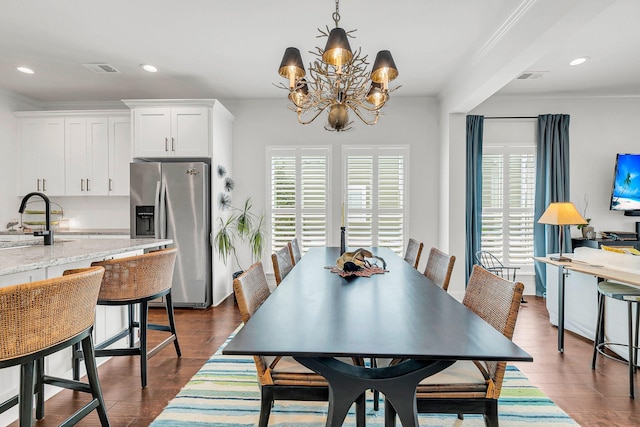 dining area featuring dark wood-type flooring, ornamental molding, a chandelier, and sink